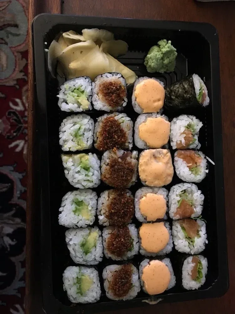 Assorted sushi rolls, ginger, wasabi in a black takeout container.