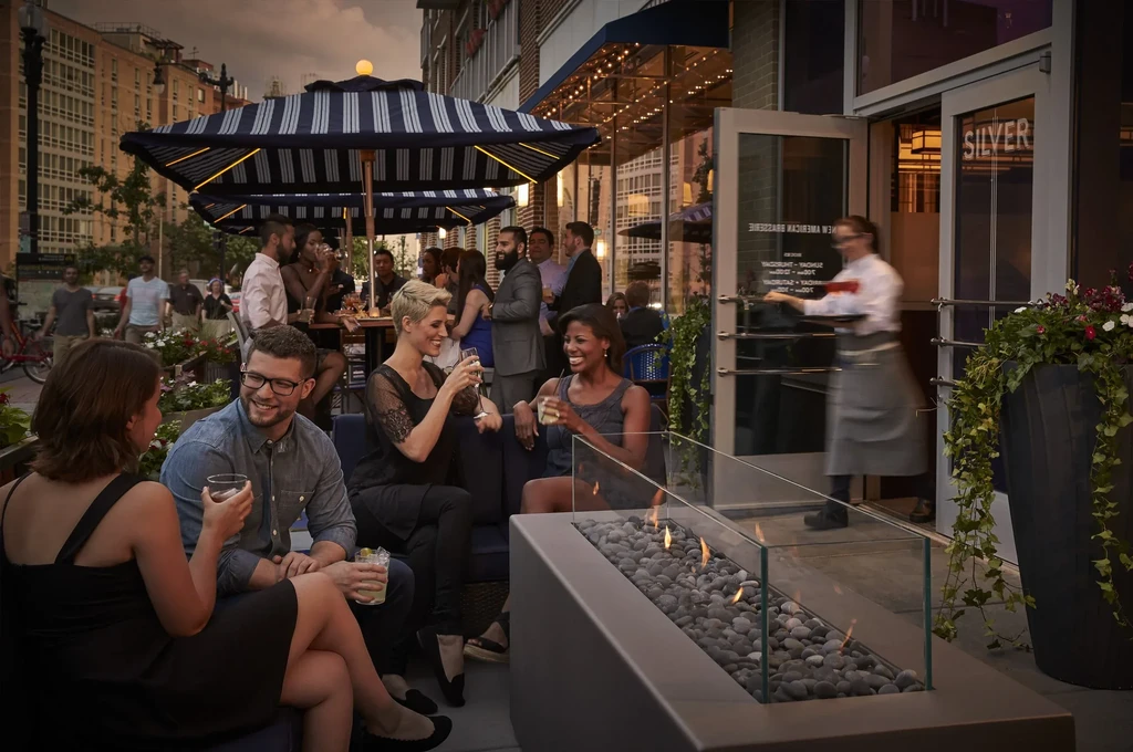 Lively outdoor brasserie at dusk; people socialize, smiling with drinks.