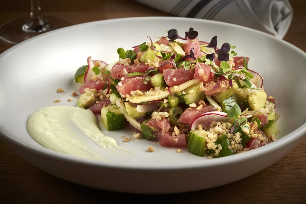 Vibrant plated poke-style dish with red fish, cucumber, quinoa, sauce.