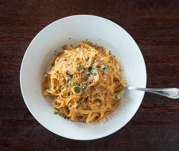 Pasta with red sauce, cheese, herbs, fork in white bowl.