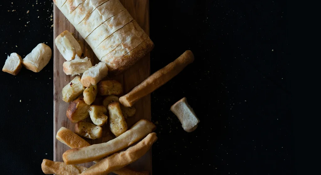 Overhead of sliced ciabatta, rustic bread pieces, and breadsticks on a board.