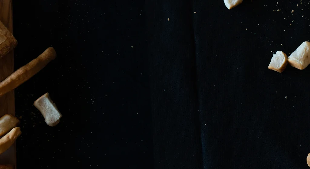 Top-down: Torn bread chunks, a breadstick, and crumbs on dark surface.