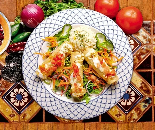 Plated enchilada-like rolls with sauce, rice, lettuce, and fresh produce.