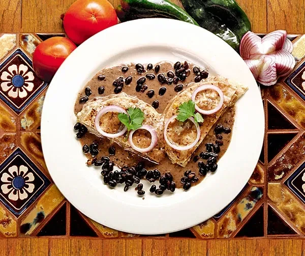 Two enchiladas with dark black bean sauce, red onion, cilantro.