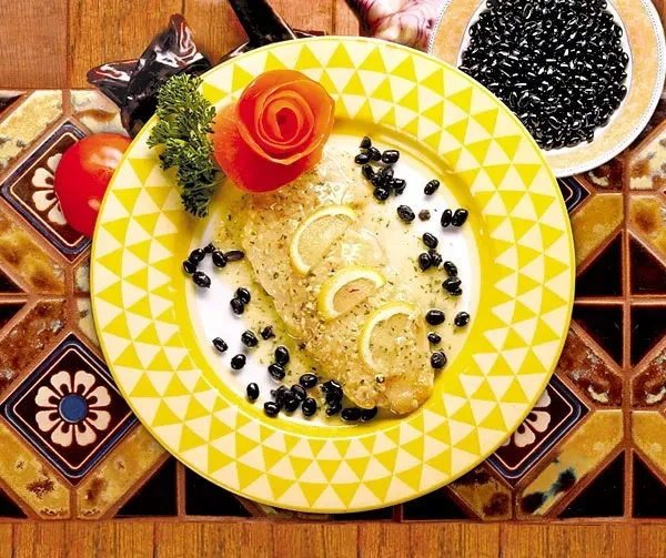 Pan-seared fish, lemon, capers, and a rose on yellow plate.