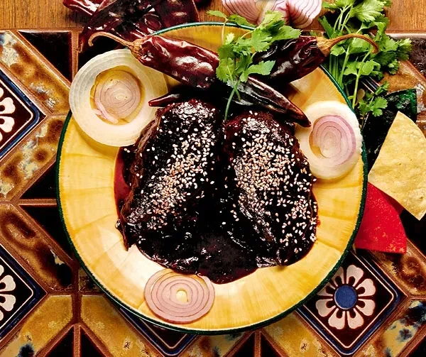 Dark mole dish with sesame seeds, cilantro, red onion on yellow plate.