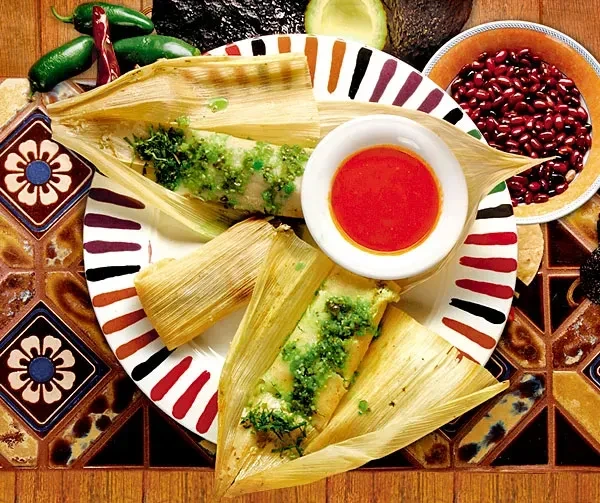 Overhead: Tamales with green sauce, red sauce, and ingredients on striped plate.