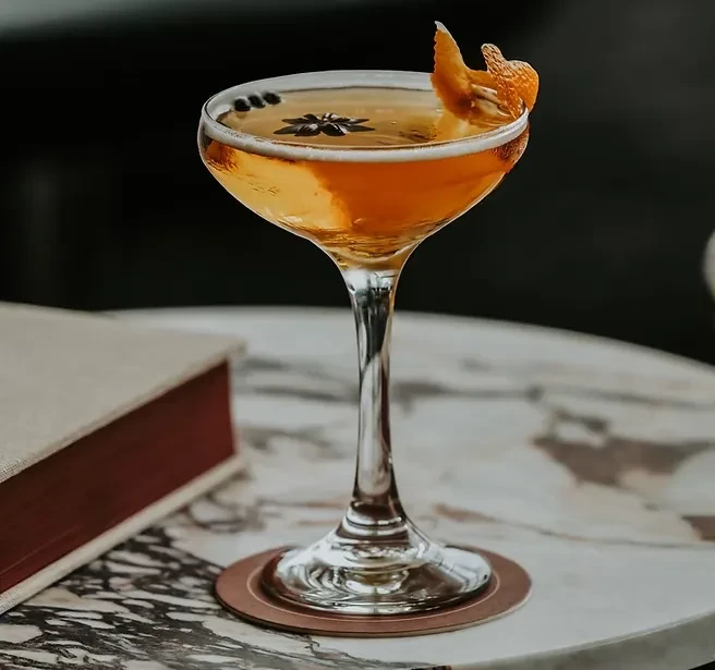 Amber cocktail in coupe glass, orange peel, star anise, on marble.
