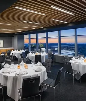 Elegant restaurant interior, set tables, panoramic city view at sunset.