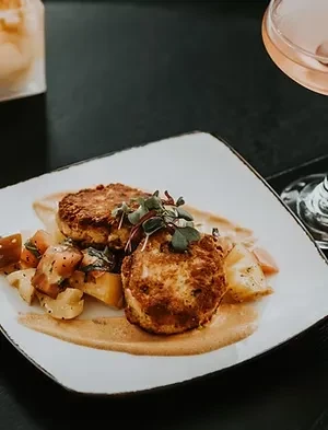 Two pan-fried patties garnished with microgreens, diced potatoes, and sauce.