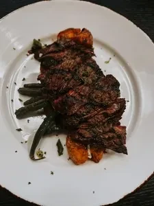 Grilled dark meat, roasted potatoes, and green vegetables on a white plate.