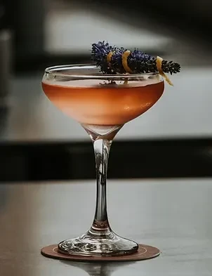 Two-tone cocktail in coupe glass, garnished with lavender and citrus peel.