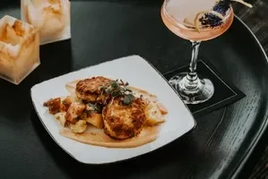 Seared food on a plate with pink cocktail, herbs, and soft candlelight.