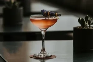 Amber-red gradient cocktail in coupe glass, garnished with dried lavender.