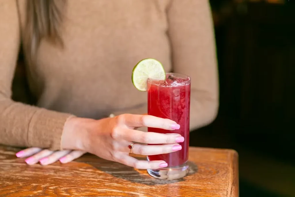 Close-up of a woman's hand holding a red drink, garnished with lime.