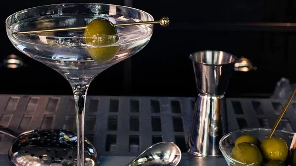 Clear martini glass with green olive on a metallic bar.