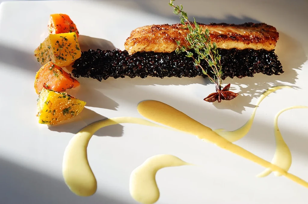 Pan-seared fish, dark rice, root vegetables, and sauce on a white plate.