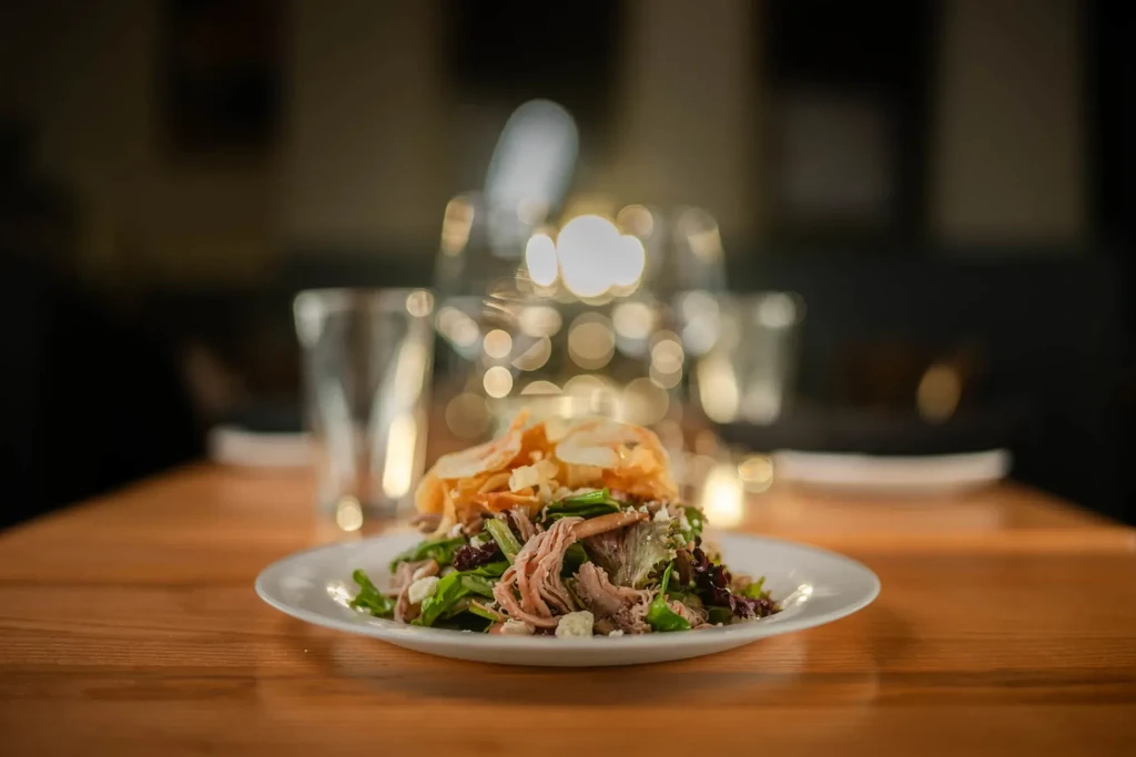 Plated salad of pulled meat, lettuce, cheese, and crisps.