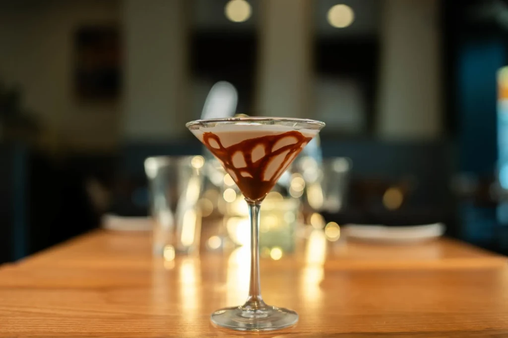Martini glass with creamy drink and chocolate drizzle on a wooden table.