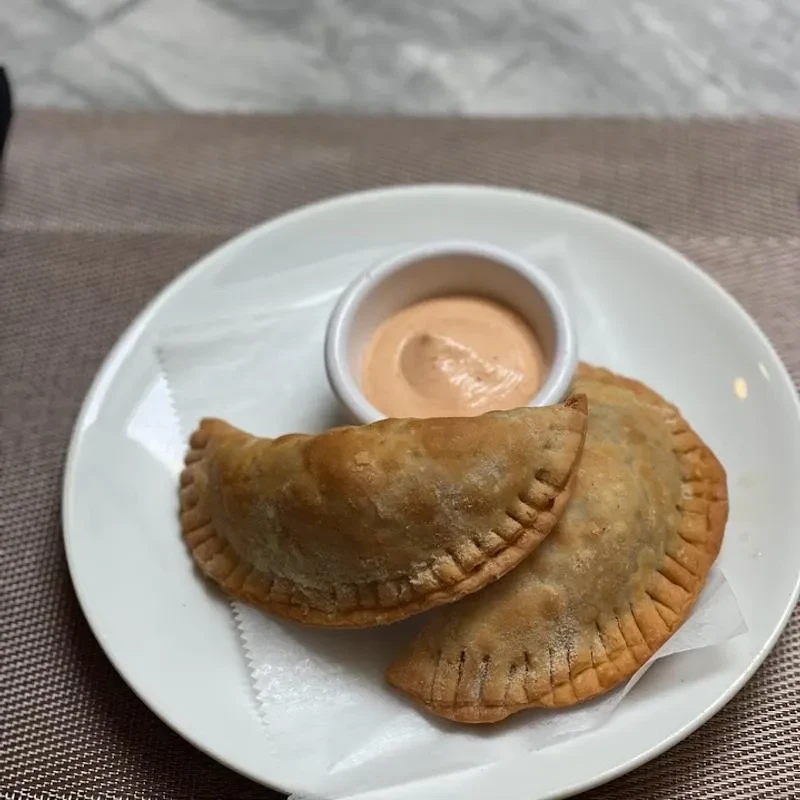 Two golden-brown empanadas with pink dipping sauce on a white plate.