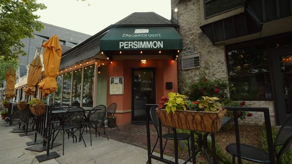 Persimmon Bistro exterior with green awning, string lights, and outdoor patio.