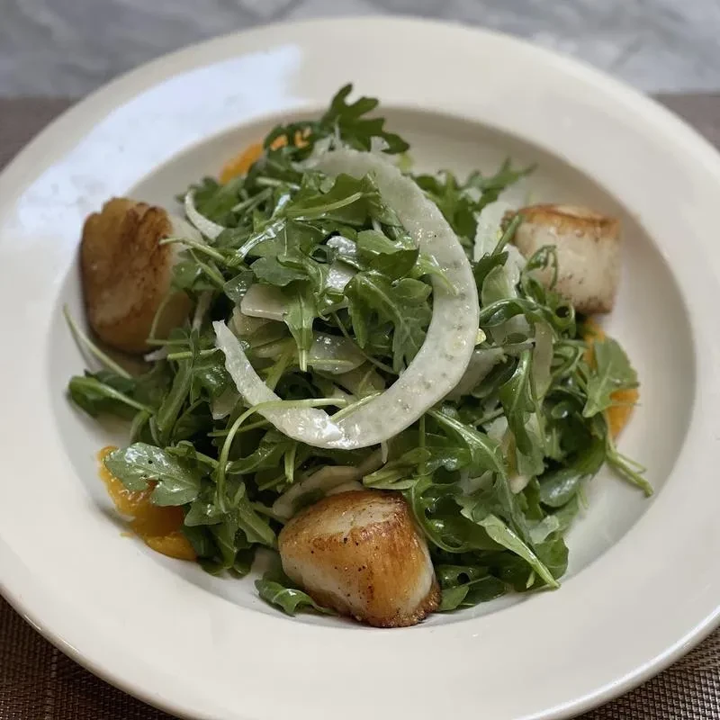 White bowl of salad with seared scallops, greens, sliced fennel, and orange.