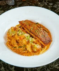 Golden-brown salmon fillet on creamy reddish pasta, garnished with chives.