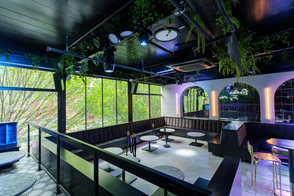 Empty chic restaurant with dark booths, hanging foliage, and mirrored arches.