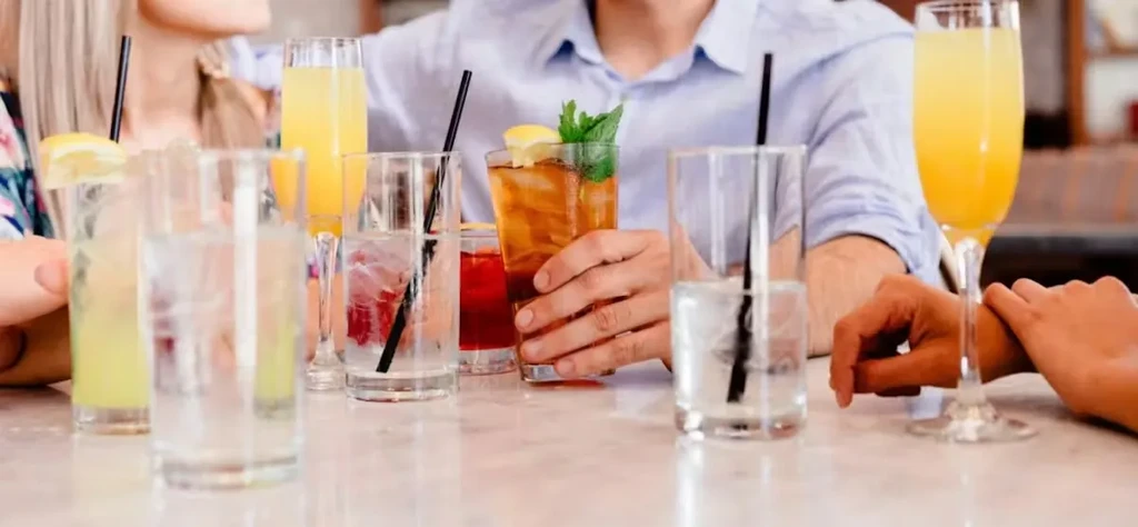 Several hands holding various colorful drinks on a table.