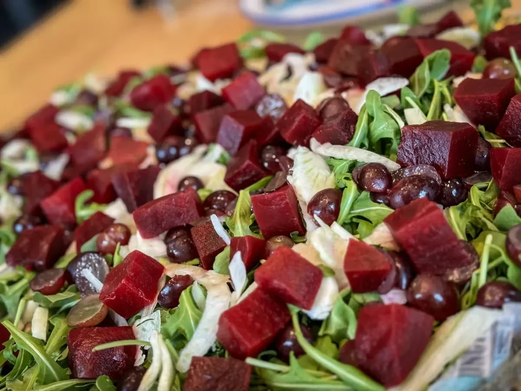 Colorful salad with red beets, green arugula, purple grapes, and shredded elements.