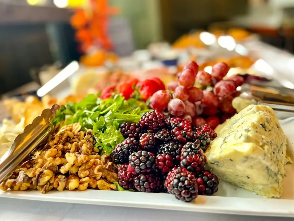 Close-up food platter with walnuts, arugula, blackberries, grapes, blue cheese, tongs.