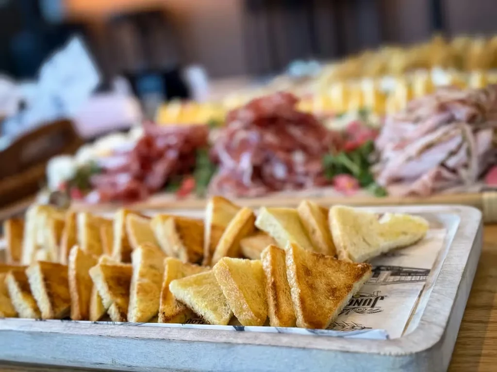 Golden-brown toasted bread triangles, with blurred charcuterie meats and appetizers behind.