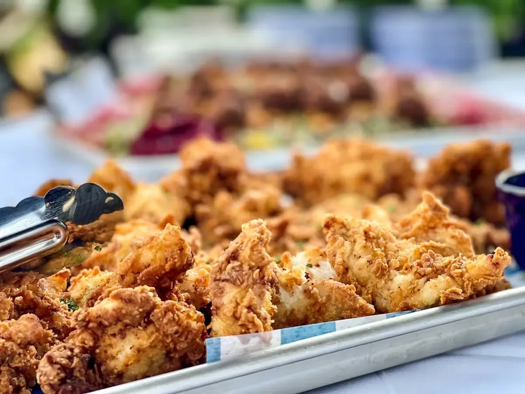 A tray of golden-brown fried chicken with tongs at a buffet.