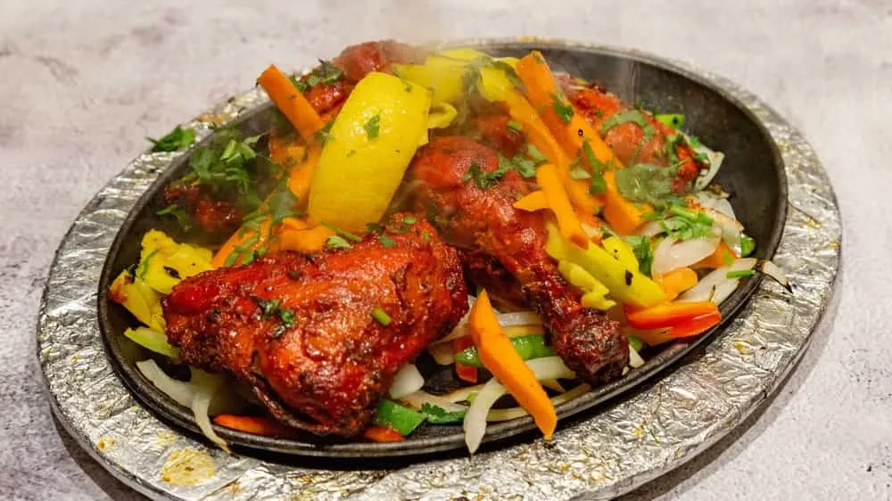 Spiced chicken, colorful vegetables, herbs, and lemon sizzling on a platter.