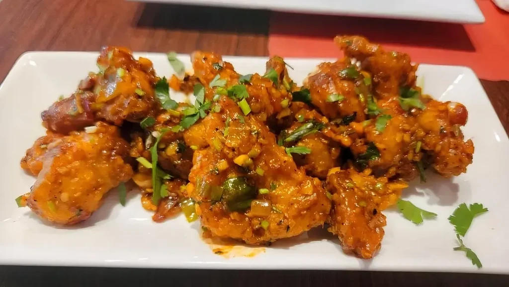 Savory red-orange dish with glossy sauce, chilies, sesame, cilantro.