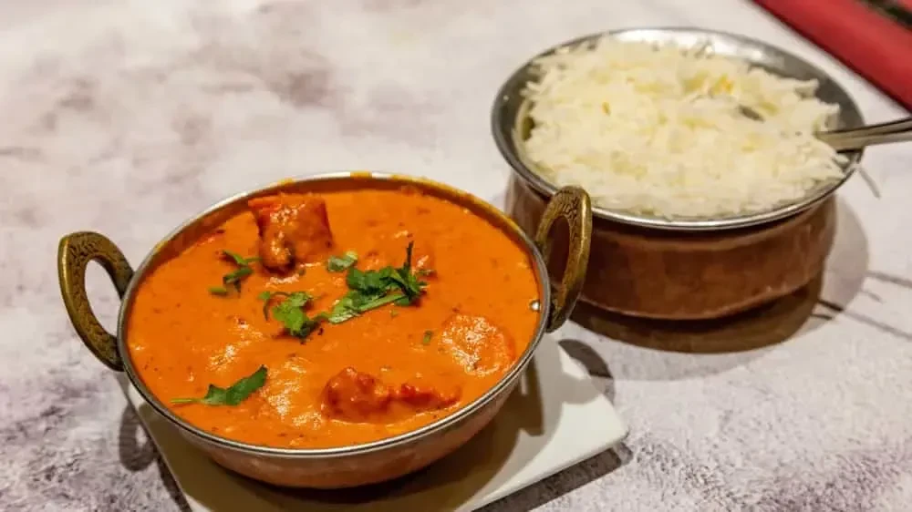 Two metal bowls of Indian curry with cilantro and fluffy basmati rice.