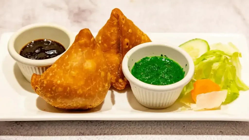 Two crispy samosas with dark and green chutneys and a side salad.
