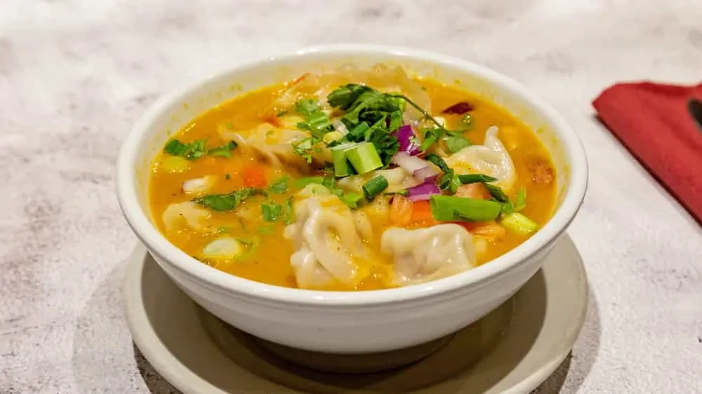 Orange-yellow dumpling soup garnished with green onions and carrots.