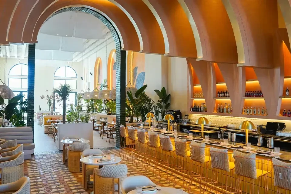 Stylish restaurant interior with terracotta arches, green plants, and golden bar.
