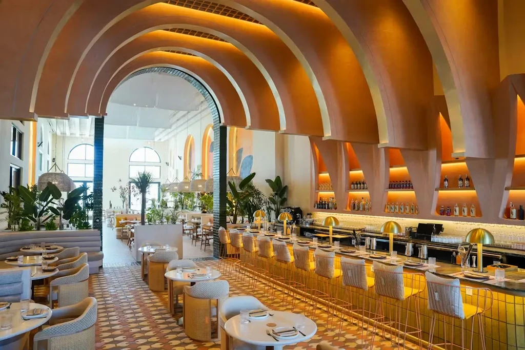 Restaurant interior with prominent orange arched ceiling, long bar, and plants.