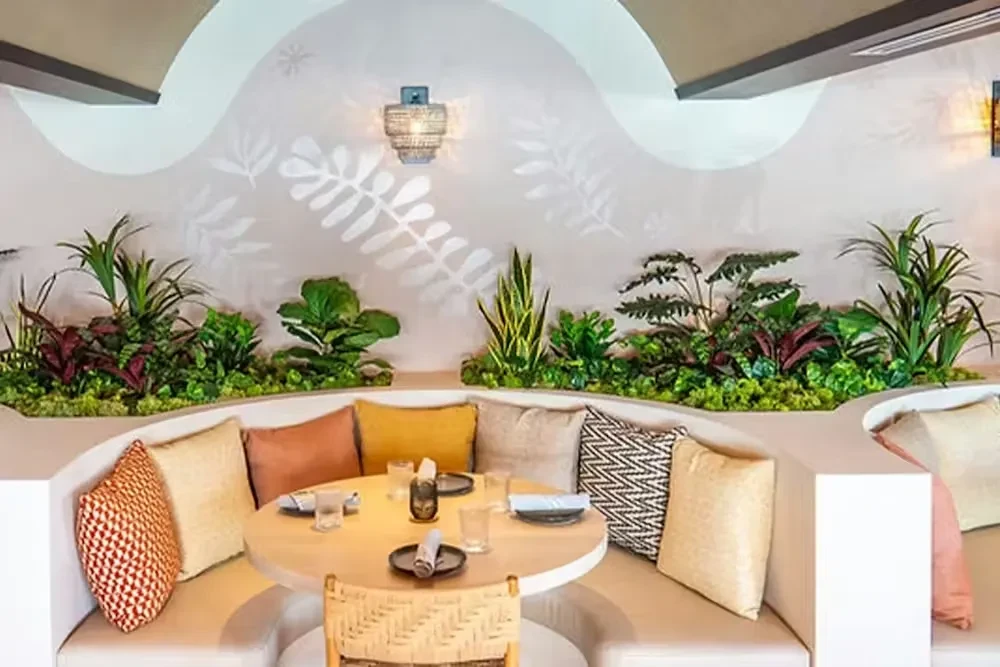 Empty modern restaurant with curved booth, set table, and botanical decor.