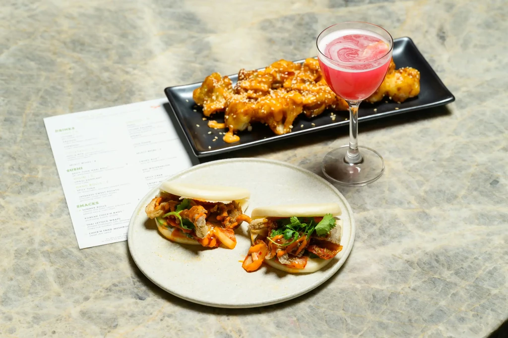 Table with bao buns, crispy cauliflower, and a pink cocktail.