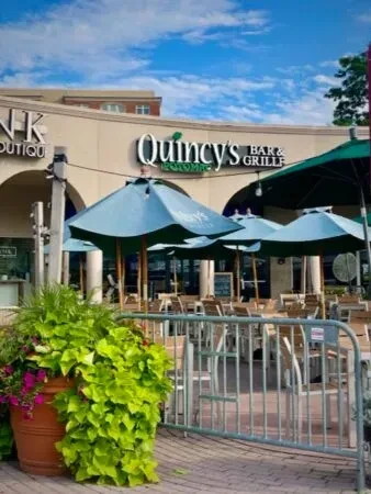Quincy's Bar & Grille exterior, sunny empty patio with blue umbrellas.