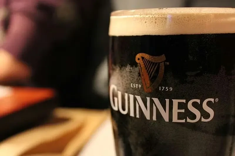 Cold pint of dark Guinness beer with creamy head and logo.