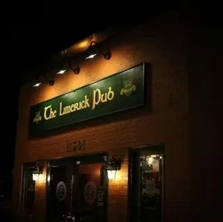 The Limerick Pub's illuminated green sign on a brick building at night.