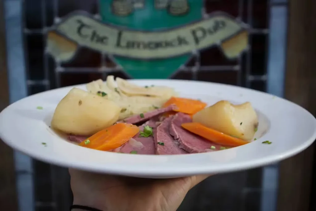 Hand holding corned beef, potatoes, carrots on a plate at Limerick Pub.