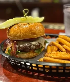 Gourmet burger, pickle spear, and fries in a black basket.