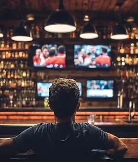 Person at a dimly lit sports bar with TVs and liquor bottles.