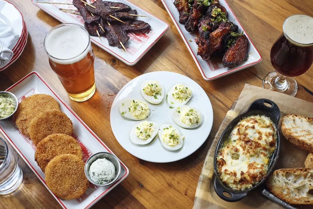 Overhead view of a wooden dining table with various appetizers and beers.