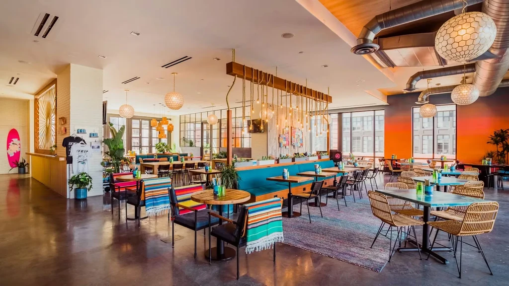 Eclectic restaurant interior featuring varied seating, industrial decor, and a pink surfboard.